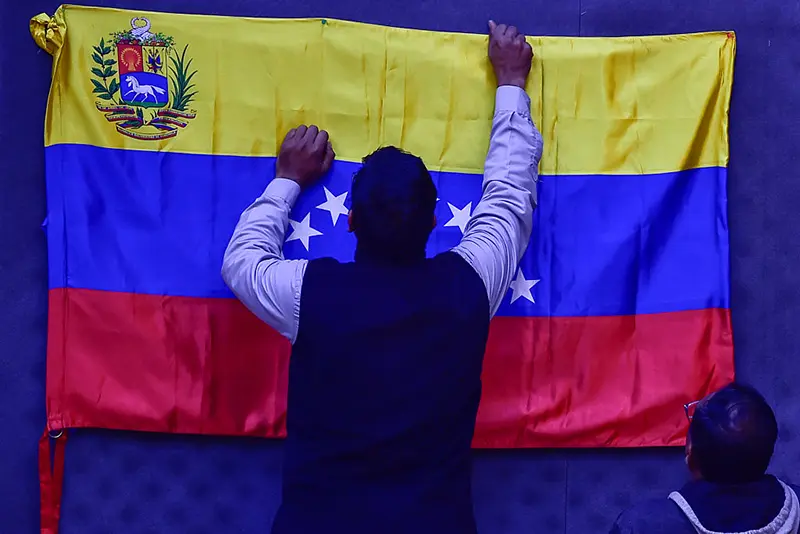 A man puts up the national flag of Venezuela during a public meeting and protest against U.S. Actions In Venezuela on January 12, 2026 in New Delhi, India. (Photo by Ritesh Shukla/Getty Images)